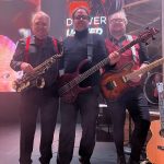 two men carrying electric guitas and one carrying a saxophone