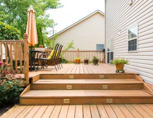 Ourdoor deck with steps and a patio table connected to the back of a house.