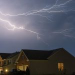 Lightning strikes in the night sky above a house