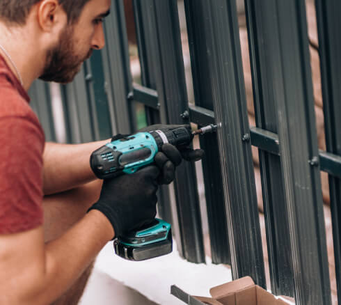 Fence worker installing metal fence using electric screwdriver