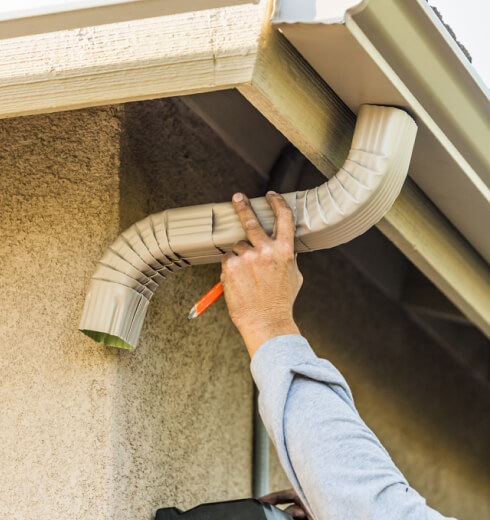 Worker attaching aluminum rain gutter spout on house exterior