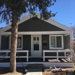 small house with a porch and a lush green tree in the front yard