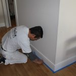 worker putting blue painter's tape at the bottom of a wall