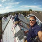 man posing for a selfie on top of a roof while repairs are in progress