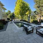 Modern backyard with a rectangular pool surrounded by lounge chairs and large trees