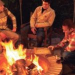 three men sitting around a firepit at night